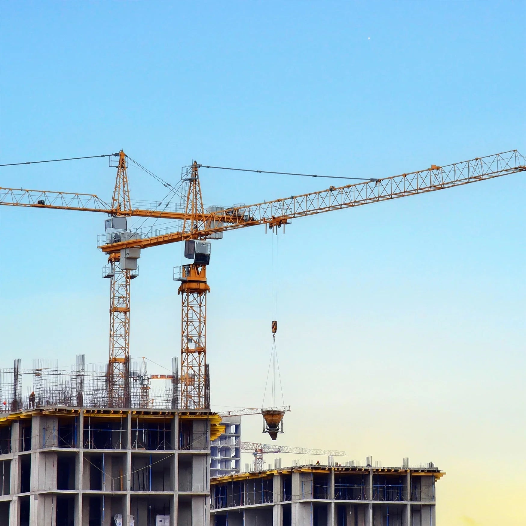 Tower cranes at a construction site with partially built concrete buildings under blue sky